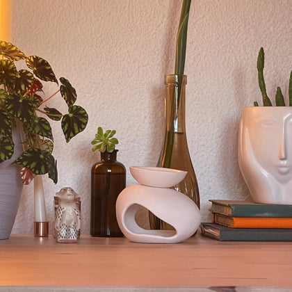 Elegant ceramic wax burner showcased on a wooden shelf with decorative plants, books, and minimalist elements, highlighting its modern design.